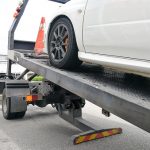 Broken down auto vehicle car towed onto flatbed tow truck with hook and chain